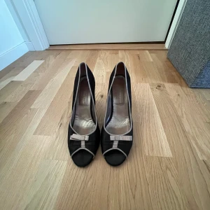 Svarta pumps med rosett  - Snygga svarta pumps med beige kant och söt rosett framtill. Skorna har öppen tå och en medelhög klack