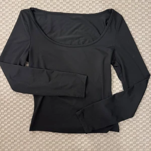 Svart långärmad topp med rund hals - En stilren svart långärmad topp med rundad halsringning. Modellen är figurnära och har en enkel, clean look som funkar till många olika outfits. Materialet känns mjukt och stretchigt, perfekt för dig som gillar minimalistisk stil.