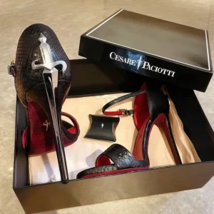 Svarta pumps från Cesare Paciotti - Exklusiva svarta pumps med hög klack från Cesare Paciotti. Skorna har ett unikt svärd-detalj på hälen, röd innersula och reptilmönstrad yta. Smal ankelrem med spänne och öppen tå ger en edgy och lyxig vibe. Perfekt för dig som gillar statement pieces.