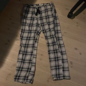 Rutiga mjukisbyxor med snörning - Säljer ett par rutiga mjukisbyxor i blått, vitt och grått med svart snörning i midjan. Byxorna är raka i modellen och har en avslappnad passform, perfekta för chill dagar hemma.