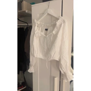 Vit croppad blus med volang - Säljer en vit croppad blus från Gina Tricot med långa ärmar, volangdetaljer vid halsringningen och ärmsluten samt knyt framtill. Perfekt för en romantisk look och passar till både jeans och kjol.