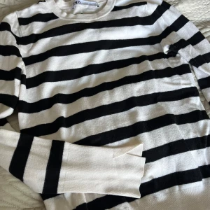 Randig svartvit tröja från Zara - Snygg stickad tröja från Zara i svart och vitt med breda horisontella ränder. Tröjan har rund halsringning, långa ärmar och ribbade muddar. Perfekt för dig som gillar klassisk stil med en modern twist.