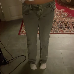 Grå bootcut jeans med stjärna - Säljer ett par grå jeans med bootcut passform och låg midja. Jeansen har en snygg stjärndetalj på bakfickan och klassisk femficksdesign. Materialet är jeans och färgen är mörkgrå, vilket ger en cool vibe. Perfekt för dig som gillar unik stil.