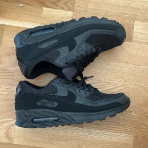Svarta Nike Air Max 90 sneakers - Säljer ett par helsvarta Nike Air Max 90 sneakers i storlek 42. Skorna har en klassisk siluett med mesh och syntetdetaljer, samt den ikoniska Air Max-dämpningen i sulan. Perfekta för dig som gillar en stilren och sportig look.