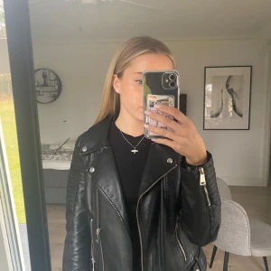 Svart skinnjacka från Vero Moda - Snygg svart skinnjacka från Vero Moda med silvriga dragkedjor och knappar. Jackan har klassisk bikerstil med bred krage, quiltade detaljer på axlar och ärmar samt flera fickor med dragkedja. Perfekt för en edgy look.