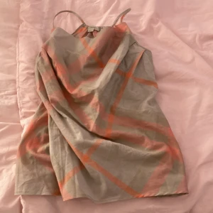 Beige och orange rutig linnetopp Burberry - Säljer en snygg linnetopp från Burberry i beige med orange och grått rutmönster. Toppen har tunna axelband och en lös, draperad passform som ger en cool och avslappnad look. Perfekt för dig som vill sticka ut med ett klassiskt men färgstarkt mönster! 😍😍😍 