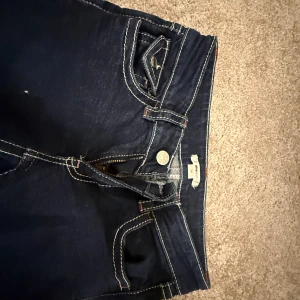 Mörkblå jeans med kontrastsömmar - Snygga mörkblå jeans från Gina Tricot med tydliga vita kontrastsömmar och coola fickdetaljer med lock och knapp. Klassisk femficksmodell och dragkedja framtill. Perfekta för en chill och trendig look.