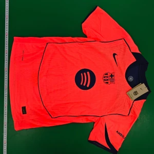 Orange FC Barcelona fotbollströja Nike - Säljer en grymt snygg orange FC Barcelona fotbollströja från Nike med mörkblå detaljer och tryck. Tröjan har korta ärmar, rund hals och är tillverkad i lätt, ventilerande material. Perfekt för dig som vill sticka ut på planen eller på läktaren.