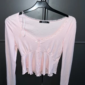 Ljusrosa blus med spets från Gina Tricot - Supersöt ljusrosa blus från Gina Tricot i storlek XS. Blusen har långa ärmar, spetsdetaljer runt halsringningen och framtill, samt en liten rosett. Den är croppad med volangkant nedtill och har en feminin, romantisk vibe.