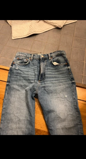 Blå ripped jeans från Zara, strl 36 - Snygga blå jeans från Zara i storlek 36 med raka ben och slitna detaljer på knä och lår. Klassisk femficksmodell med hög midja och coolt vintage-tvättad look. Perfekta för dig som gillar en avslappnad och trendig stil.
