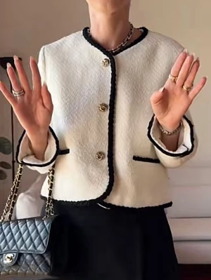 Vit kavaj med svarta detaljer - Snygg vit kavaj med svarta kanter och guldfärgade knappar framtill. Jackan har en klassisk, rak form och är långärmad med svarta detaljer vid fickor och ärmslut. Materialet är strukturerat och känns lyxigt, perfekt för en chic look.