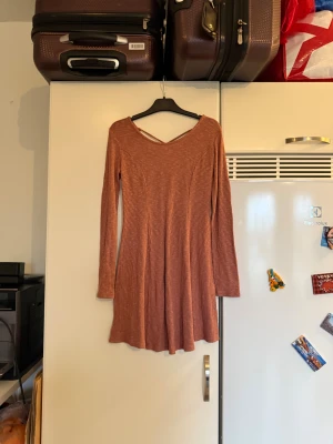 Rosa ribbad kortklänning med lång ärm - Superfin kort klänning i en dämpad rosa nyans med ribbat tyg och lång ärm. Klänningen har en lätt utställd kjol och snygg v-ringning med dekorativ detalj i ryggen. Perfekt för dig som gillar en enkel men trendig look. Storlek M. Mycket fint skick, jag hittar inga synliga anmärkningar eller defekter. 