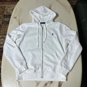 Ralph Lauren vit zip hoodie - Säljer denna vita hoodien då den var för stor på mig. Jag är 172cm och 75kg. Annars är den helt ny och bara använd en gång!. Taggen är också fortfarande på den.