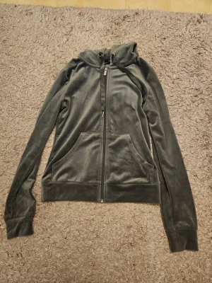 Mjuk och skön mörkgrå velourhoodie från Gina Tricot XXS - Jättefin och jättemjuk och skön mörkgrå hoodie från Gina Tricot i velourmaterial. Tröjan har huva med snörning, dragkedja framtill och två stora fickor. Långärmad och med breda muddar vid ärmslut och nederkant. Nyprid runt 200-300 kr. Säljer då jag inte får användning för den längre, men den är jättemjuk och skön att ha när det blir kallt. Mycket bra skick, endast använd väldigt få gånger.