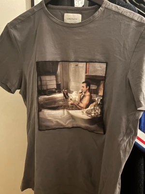 Grå Limitato t-shirt med konstmotiv - Snygg grå t-shirt från Limitato med ett stort konstnärligt tryck framtill, inspirerat av Terry O'Neill. Klassisk rund hals och korta ärmar. Materialet är mjuk bomull som känns skönt mot huden. Perfekt för dig som gillar unika och coola prints.