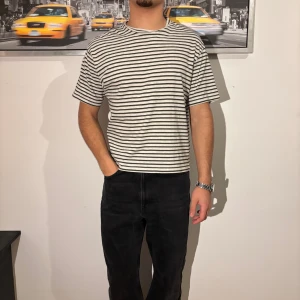 Vit och svart randig t-shirt - Säljer en vit t-shirt med svarta horisontella ränder. Modellen har en klassisk rund hals och korta ärmar. Passformen är normal och materialet känns som mjuk bomull, perfekt för en chill och stilren look.