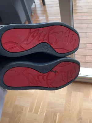 Blåa  Christian Louboutin - Säljer ett par blåa sneakers från Christian Louboutin med ikoniska röda sulor och diskret broderad logga på hälen. Skorna har snörning, rund tå och är tillverkade i mocka med en platt sula. Perfekt för dig som vill ha en lyxig och stilren look. Box medföljer äkta! Billigt pga lite sliten