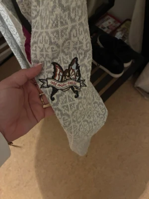 Odd Molly mönstrad kofta med rosett - Superfin ljusgrå och vit kofta från Odd Molly med snyggt mönster och broderad logga på ärmen. Koftan har lång ärm, två fickor och en mörklila rosett framtill som knytning. Perfekt för dig som gillar detaljer och vill ha en unik look.