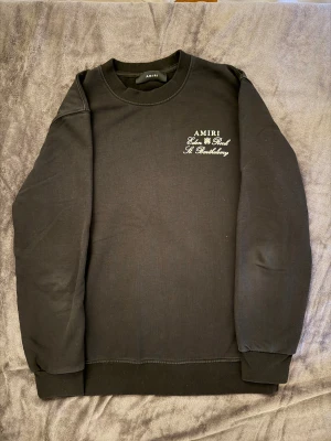 Svart sweatshirt från Amiri med tryck - Svart sweatshirt från Amiri med stilrent tryck på bröstet och stort grafiskt tryck på ryggen. Tröjan har rund hals, långa ärmar och ribbade muddar. Materialet är mjuk bomull som känns skönt mot huden. Perfekt för dig som gillar streetwear med exklusiv vibe. Passar bäst som M