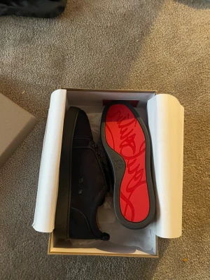 Christian Louboutin blåa sneakers - Säljer ett par blåa sneakers från Christian Louboutin med signatur röd sula och broderad logga på hälen. Skorna har snörning och är tillverkade i mocka med en platt sula. Snygg och stilren design med exklusiv känsla, perfekt för dig som gillar lyxiga detaljer.