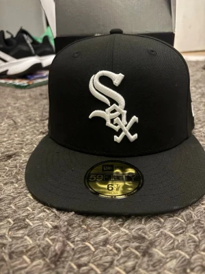 Svart White Sox 59FIFTY keps från New Era - Helt ny snygg svart 59FIFTY keps från New Era med White Sox-logga broderad i vitt framtill och MLB-logga baktill. Klassisk flat brim och stilren design. Insidan har märkning och etikett. Perfekt för dig som gillar sportig streetstyle.  Säljer för jag köpte två och glömde lämna tillbaka en av dem