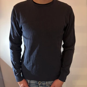 Mörkblå stickad tröja från Bläck - En stilren mörkblå stickad tröja från Bläck i storlek S. Tröjan har rund halsringning, ribbade muddar och är långärmad. Perfekt för lager-på-lager och enkel att matcha med jeans.