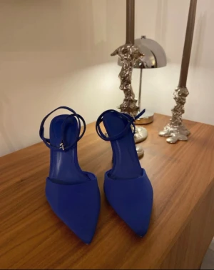 Koboltblå pumps med smal klack, stl 37 - Säljer ett par trendiga koboltblå pumps med spetsig tå och smal hög klack. Skorna har en elegant ankelrem med spänne och är tillverkade i ett slätt material som ger en stilren look. Perfekta för att lyfta vilken outfit som helst.