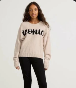 Beige stickad tröja med svart text - Säljer en beige stickad tröja från Iconic med svart broderad text över bröstet. Tröjan har rund hals, ribbade muddar och lång ärm. Passformen är loose och den är lite croppad i modellen. Perfekt för dig som gillar statement-plagg