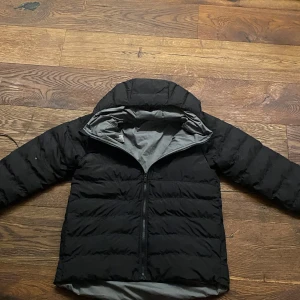 Svart och grå dunjacka från The North faceFace - Säljer en dunjacka från The North Face med huva och dragkedja. Jackan är svart på ena sidan och grå på andra, vilket gör den vändbar. Den har en clean look med logga på bröstet och är perfekt för kalla dagar. Passformen är normal och jackan är långärmad. Jackan är k storlek 164. Ny pris 1395kr 