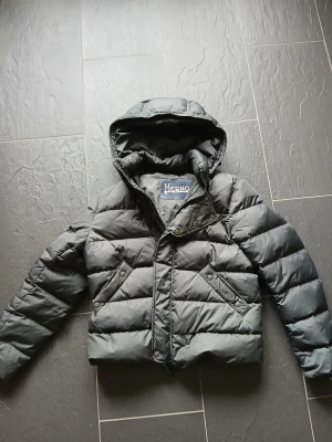 Svart pufferjacka från Herno - Säljer en svart pufferjacka från Herno med huva, dragkedja och tryckknappar framtill. Man kan ta av hyllan. Strolek s. Grå/svart färg. 