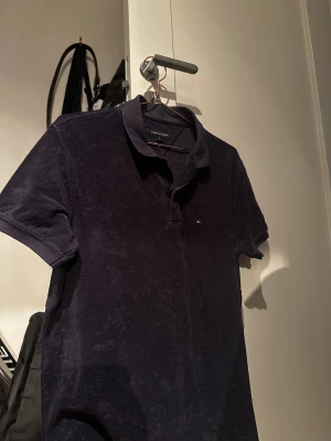 Mörkblå piké från Tommy Hilfiger - Säljer en mörkblå pikétröja från Tommy Hilfiger i regular fit. Skjortan har klassisk krage, korta ärmar och liten broderad logga på bröstet. Materialet är mjukt och frottéliknande, perfekt för en chill och stilren look.