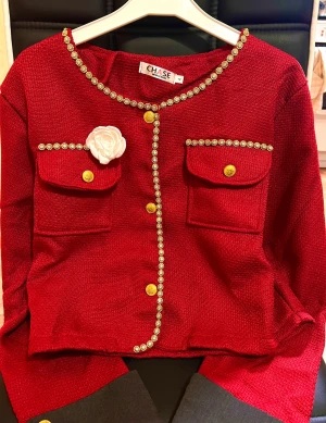 VinRöd jul set   tweed jacka  med gulddetaljer och kjol - Snygg röd  med guldfärgade knappar och dekorativa gulddetaljer längs kanterna. Jackan har två fickor framtill och en vit blomma som accessoar på bröstet. Perfekt för dig som vill sticka ut med en elegant och trendig look.