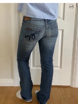 Blå bootcut jeans med broderad ficka - Säljer ett par blå jeans med bootcut passform och snygg broderad detalj på bakfickan. Jeansen har klassisk femficksdesign och är tillverkade i slitstarkt denim. Perfekta för dig som gillar en avslappnad men ändå trendig look.