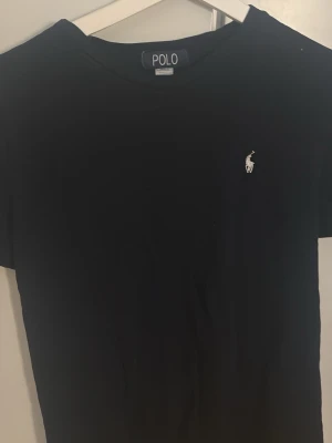 Svart t-shirt från Polo Ralph Lauren - Svart t-shirt från Polo Ralph Lauren med klassisk broderad logga på bröstet. T-shirten är i bomull och har en normal passform med korta ärmar och rund hals. Perfekt för en clean och stilren look. Jag har storlek s i tröjor och den funkar även!💞 Kan diskutera pris