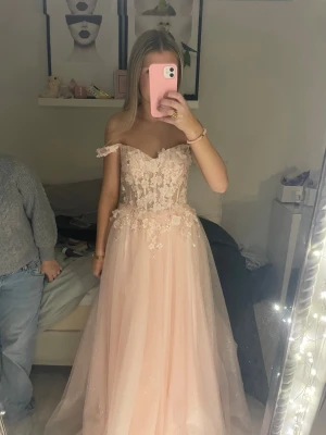 (INTRESSE KOLL) Ljusrosa långklänning med blommor  - Superfin ljusrosa långklänning med axelbandslös design och glittrigt tyg. Livet är dekorerat med 3D-blommor och spetsdetaljer som ger en romantisk känsla. Kjolen är i flera lager tyll för extra volym och flow. Perfekt till balen.Klänningen är aldrig använd och den är köpt hos aninas i Helsingborg 
