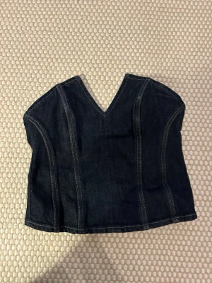 Mörkblå denim korsett-topp - Säljer en mörkblå croppad korsett-topp i denim med markerade sömmar och v-ringning framtill. Använt ett par gånger. Från Zara. Toppen är axelbandslös och har dragkedja i ryggen för enkel på- och avtagning. Perfekt att styla med jeans eller över en skjorta.
