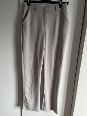 Beiga kostymbyxor med raka ben - Säljer ett par  beiga kostymbyxor från 157. Byxorna har raka ben, hög midja och bälteshällor. De är raka vid låren men går lite ut vid slutet. Har haft de på mig ett par gånger men annars ser de super bra ut.  Passar S/M 