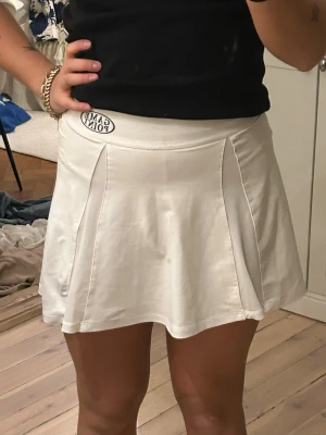 Tenniskjol från Gina Tricot XS - Supersnygg vit tenniskjol från Gina Tricot i storlek XS. Kjolen har en lätt utsvängd form och bred linning med en liten 'Game Point'-patch framtill. Tillverkad i mjuk polyesterblandning med stretch för skön passform.