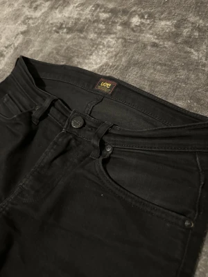 Lee Jeans - Säljer ett par svarta slim fit jeans från Lee med klassisk femficksdesign och diskret Lee-logga där bak. Jeansen har smal passform, normal midja och är gjorda i jeansmaterial. Perfekta till sneakers eller boots.