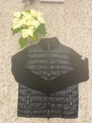 Svart Moncler cardigan M - Säljer en svart Moncler cardigan från Moncler med stickade ärmar och quiltad kropp. Cardigan har dragkedja framtill, två fickor med dragkedja. Aldrig använd skick 10/10 passar till allt! Priset går att ändra
