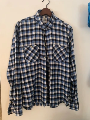 Blårutig skjorta från Vaillent Clothing - Säljer en blårutig skjorta från Vaillent Clothing i storlek Large. Skjortan har två stora bröstfickor med knappar, klassisk krage och långa ärmar. Tillverkad i mjuk bomull och perfekt för en avslappnad stil.