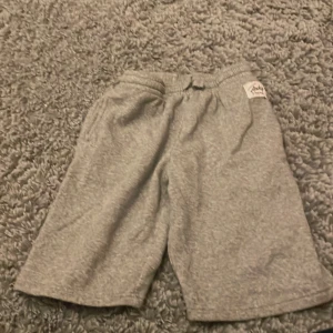 Grå mjukisshorts från Frank Dandy - Säljer ett par grå mjukisshorts från Frank Dandy med resår och snörning i midjan. Shortsen är tillverkade i mjukt bomullsmaterial och har en avslappnad passform. Perfekta för chill dagar eller när du vill vara bekväm.