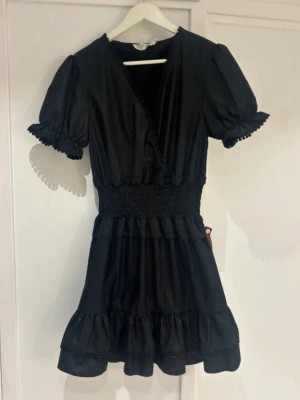 Svart omlottklänning med volanger - Säljer min supersöta svarta kortklänning från BYIC med omlottmodell, puffärmar och volangdetaljer. Är tyvärr för stor för mig, jag är 156 💕 Aldrig använt men har ingen prislapp 🤗