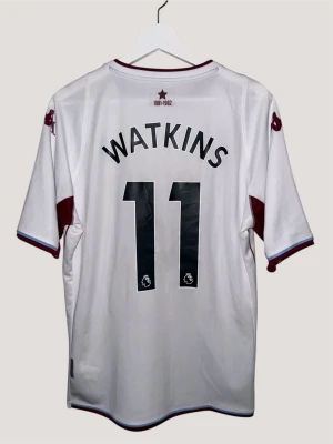 Aston Villa 21/22 Borta - #11 Watkins - Kappa fotbollströja - storlek L - 𝐀𝐬𝐭𝐨𝐧 𝐕𝐢𝐥𝐥𝐚 𝟐𝟏/𝟐𝟐 𝐀𝐰𝐚𝐲 Aston Villas bortatröja för säsongen 2021/22 har en ren vit design med subtila vinröd detaljer för en snygg, modern look. Med Watkins namn och nummer 11 på ryggen representerar den anfallarens snabbhet och avslut under en spännande Premier League-säsong för Villa 🦁🟣  Skick: 9/10. Utmärkt skick, inga synliga skador. Som ny! ✨  Storlek: L  Låt mig veta om du har några frågor eller andra funderingar. Priset är alltid förhandlingsbart och säker förpackad frakt inom 24 timmar 🚚