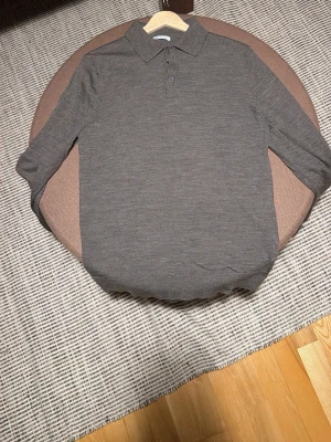 Brun långärmad pikétröja från ZARA - Säljer en stilren brun långärmad pikétröja från ZARA. Tröjan har klassisk krage och två knappar framtill. Materialet känns mjukt och lätt, perfekt för lager på lager under höst och vår. 