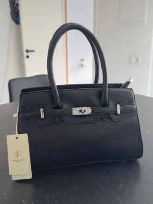 Svart handväska - SKICKA PRISFÖRSLAG!!!!Snygg svart handväska från Herisson Paris i skinnimitation med silverfärgade metalldetaljer och dubbla handtag. Väskan har ett klassiskt, stilrent utseende och kommer med avtagbar axelrem. 