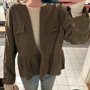 Olivgrön jacka med knappar Zara - Sååå snygg olivgrön jacka med knappar framtill och två stora fickor på bröstet. Jackan har en loose passform och är perfekt för höst och vår. Den har långa ärmar och en stilren design som passar till många olika outfits. Använd 1 gång.