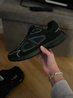 Svarta CD sneakers med reflekterande detaljer - Säljer ett par svarta sneakers från CD med reflekterande silverdetaljer och stora CD-loggor på sidorna och hälen. Skorna har snörning, platt sula och är tillverkade i en mix av mesh och syntetmaterial. Perfekta för dig som gillar streetwear och vill sticka ut.