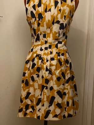 Kort ärmlös klänning från H&M 38 - halsringning och en markerad midja med utställd kjol. Stängs med dragkedja baktill. Längd: 95 cm, bystvidd: 45 cm 93% polyester, 7% elestan  Inga bilder när den sitter på mig! Katter finns i hemmet!