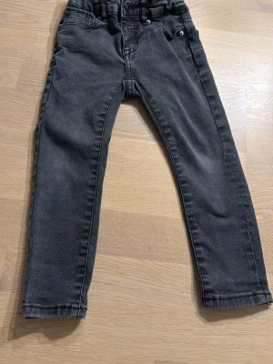 Svarta jeansbyxor från 157 strl  för barn i strl 110  - Säljer ett par svarta jeansbyxor från 157 med klassisk femficksdesign och knappgylf. Byxorna har en rak passform och är tillverkade i mjukt bomullsmaterial med lite stretch för extra komfort. 